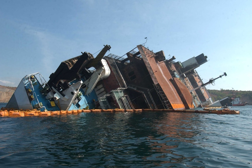 The wreck of a sinking ferry, half of the craft visible above the water.