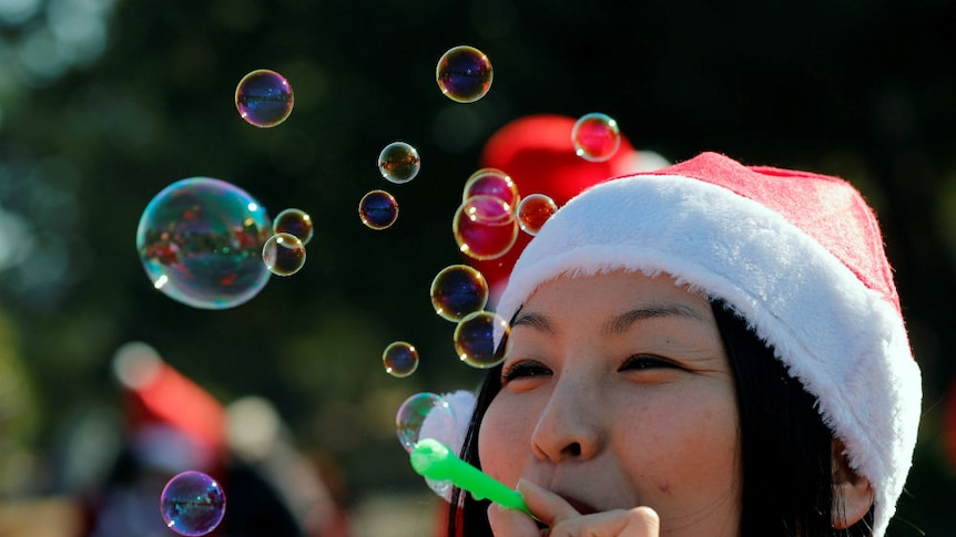 A woman dressed as Santa blows bubbles