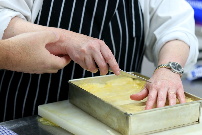 A close up photo of Sarah Elliot cutting baklava as Stephen Hoger holds her arm.