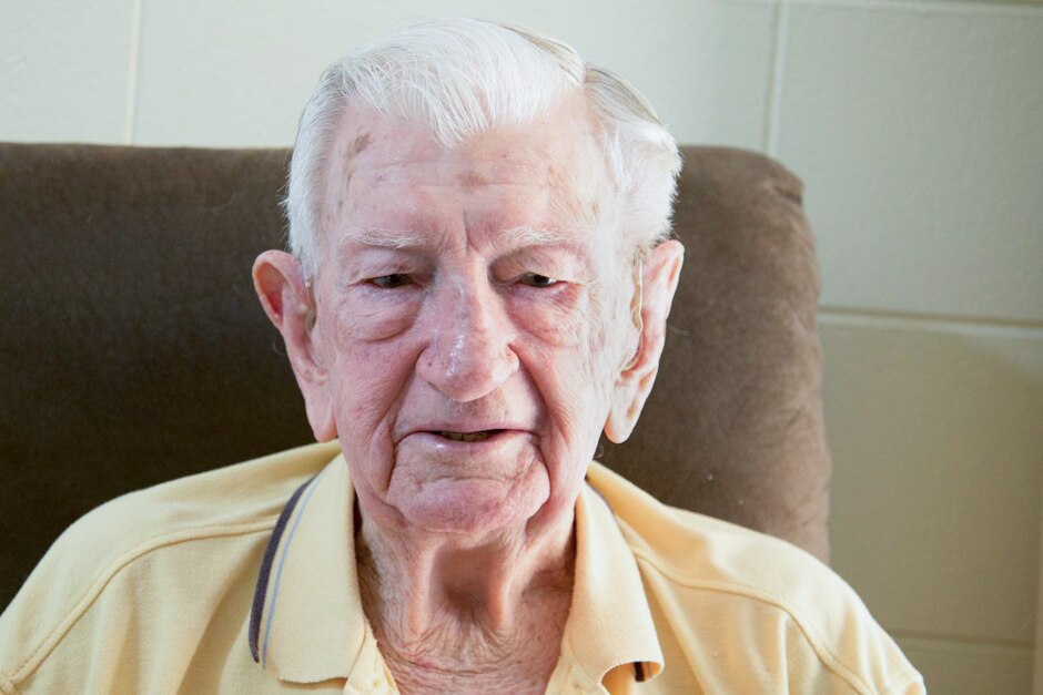 An elderly man sits in a brown chair.