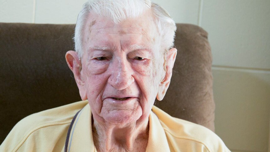 An elderly man sits in a brown chair.
