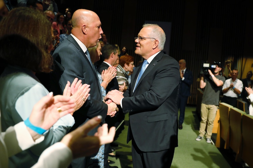 Morrison shakes Dutton's hand as he stands among a crowd of supporters at a conference centre.