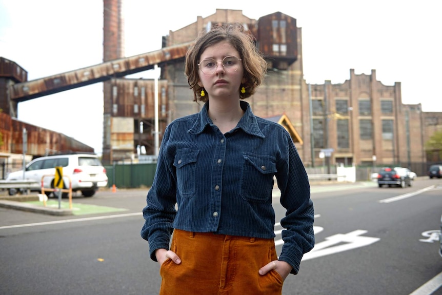 Jean Hinchliffe, standing in a street with her hands in her pockets, looks at the camera.