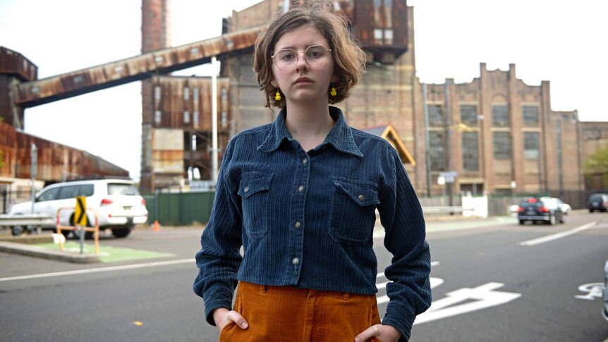 Jean Hinchliffe, standing in a street with her hands in her pockets, looks at the camera.