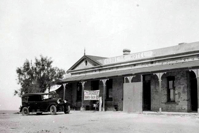 An old car parked in front of a hotel.