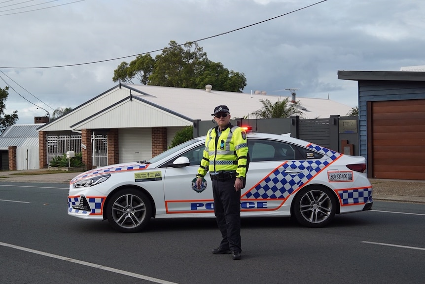 A policeman in front of a police car with sirens on in a suburban street