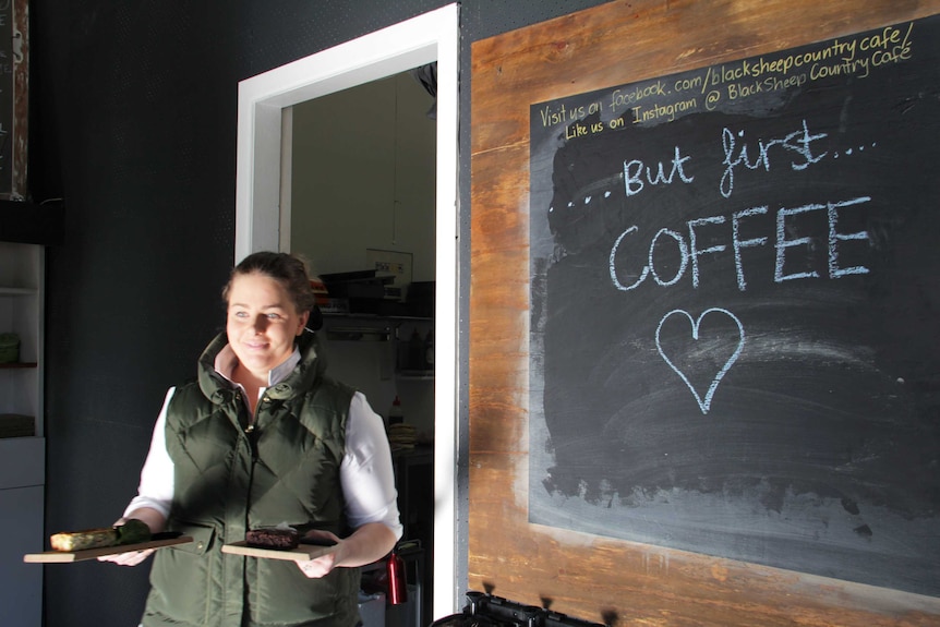 A woman carrying toast walks past a sign saying 'but first ... coffee'.