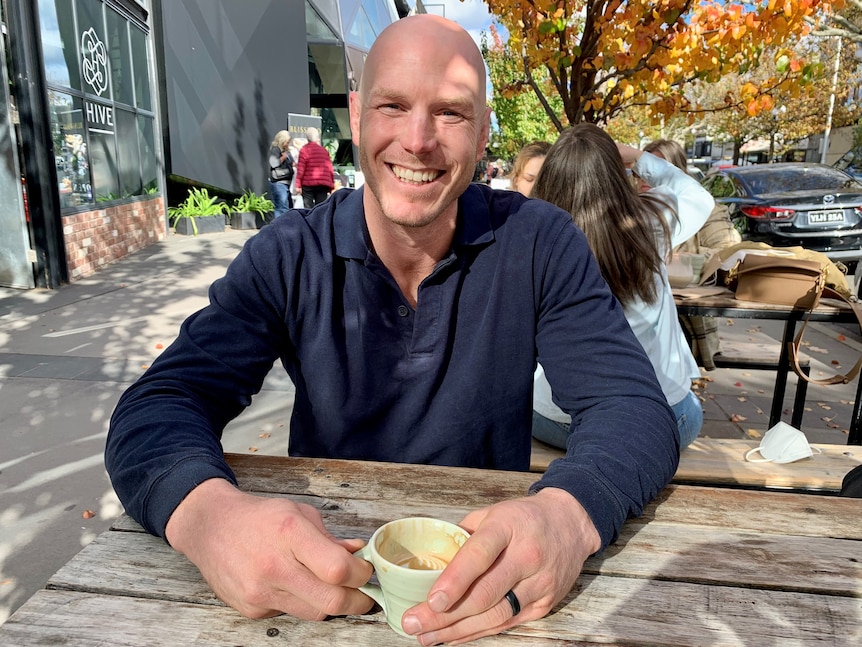 Man wearing long dark blue shirt drinking coffee. 