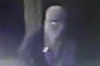 A black and white CCTV image of a hooded man