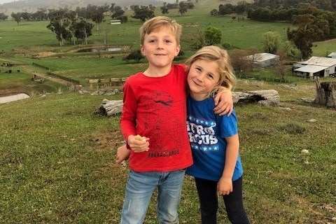 Sister and brother standing on green grass in front of viewpoint at their family farm in Tarcutta.
