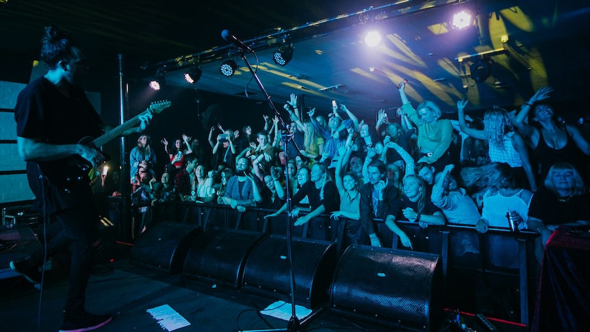 A packed front row audience enjoys a guitarist performing live on stage