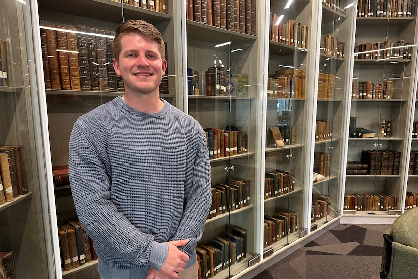 man standing smiling in front of a wall of old books