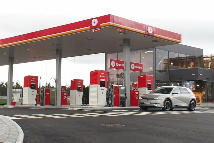 Six EV chargers at a fuel station with a sign reading 300kW