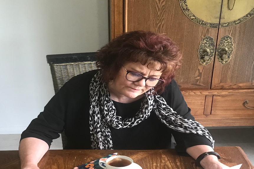 Woman sits at the kitchen table reading a letter.