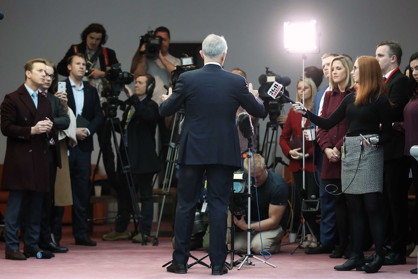 Malcolm Turnbull stands with his back to the camera. He is facing a large media pack with lights, cameras and microphones.