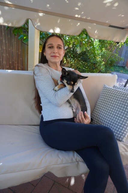 Vanessa sits on an outdoor setting, smiling while holding Ranger, a black, white and light brown chihuahua
