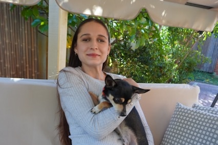 Vanessa sits on an outdoor setting, smiling while holding Ranger, a black, white and light brown chihuahua