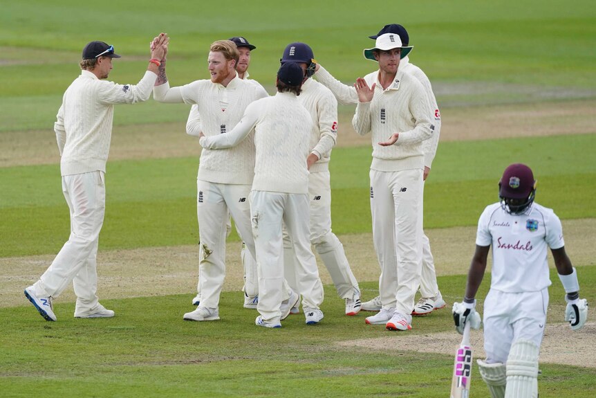Ben Stokes gives a high five to his teammates, who hug him and clap as Jermaine Blackwood walks off in the foreground