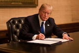 US President Donald Trump sits at a wooden desk in the Treaty Room at the White House and signs a bill