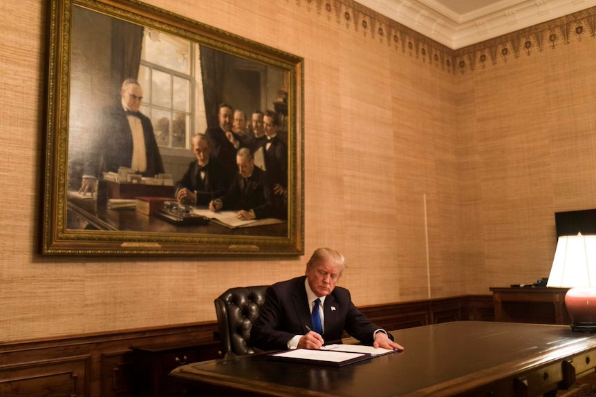 US President Donald Trump sits at a wooden desk in the Treaty Room at the White House and signs a bill