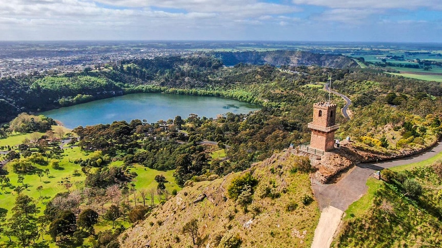 A large blue lake surrounded by sprawling grass parklands and trees, with a large brick tower in the foreground.
