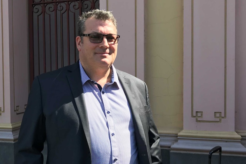 A man in a suit and sunglasses leaving a courthouse.