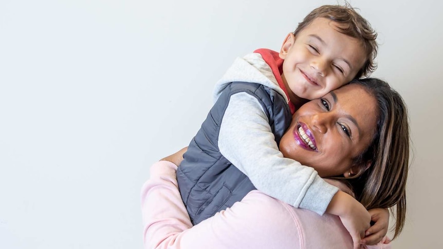 a woman holds her small child high in her arms, they are both smiling joyously towards the camera