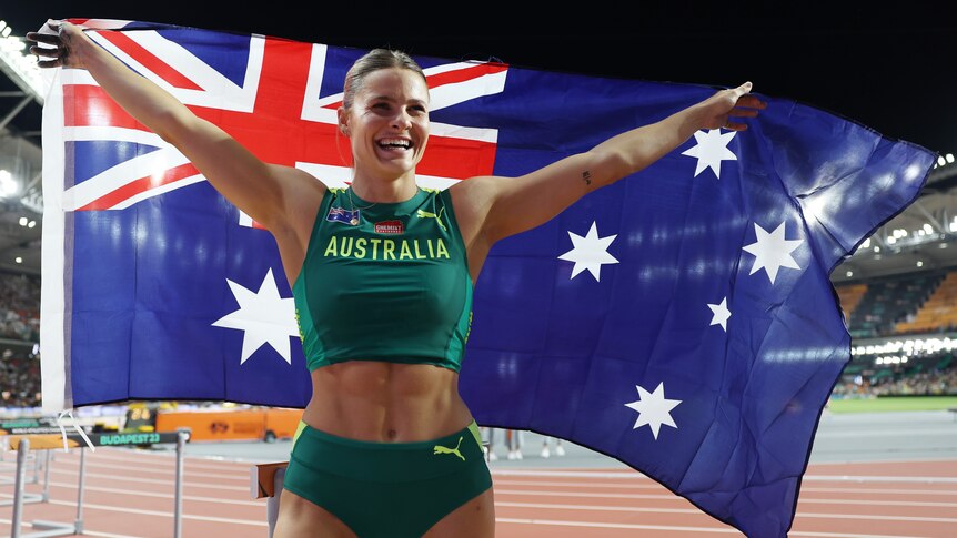 Nina Kennedy smiles and holds an Australian flag up behind her back