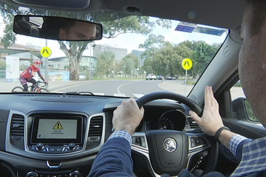 Driver at the steering wheel with cyclist visible through the windscreen.