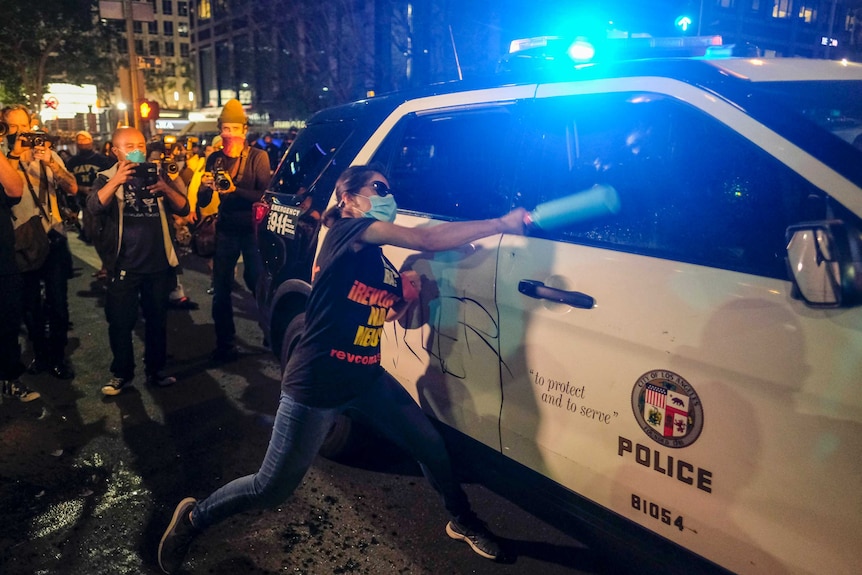 A demonstrator attacks a police car during a protest in downtown Los Angeles.