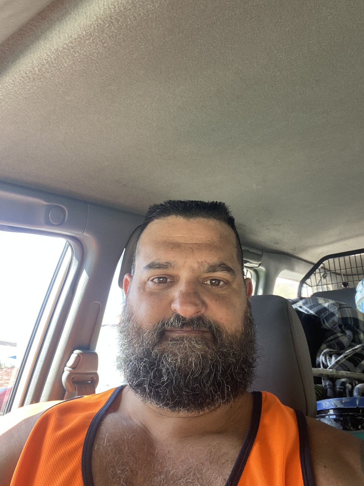 Un hombre con una espesa barba castaña y pelo corto se toma un selfie en su coche. 