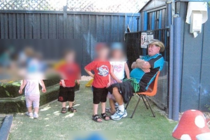 A man sits on a chair, surrounded by children