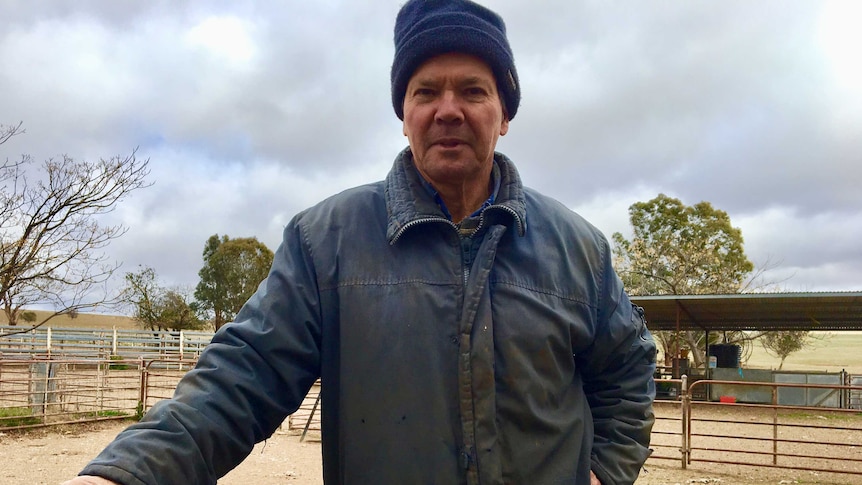 A man stands in an empty cattle yard with a grey sky above