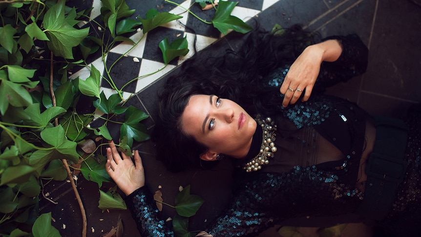 Caiti Baker lies on the tiled ground, surrounded by foliage