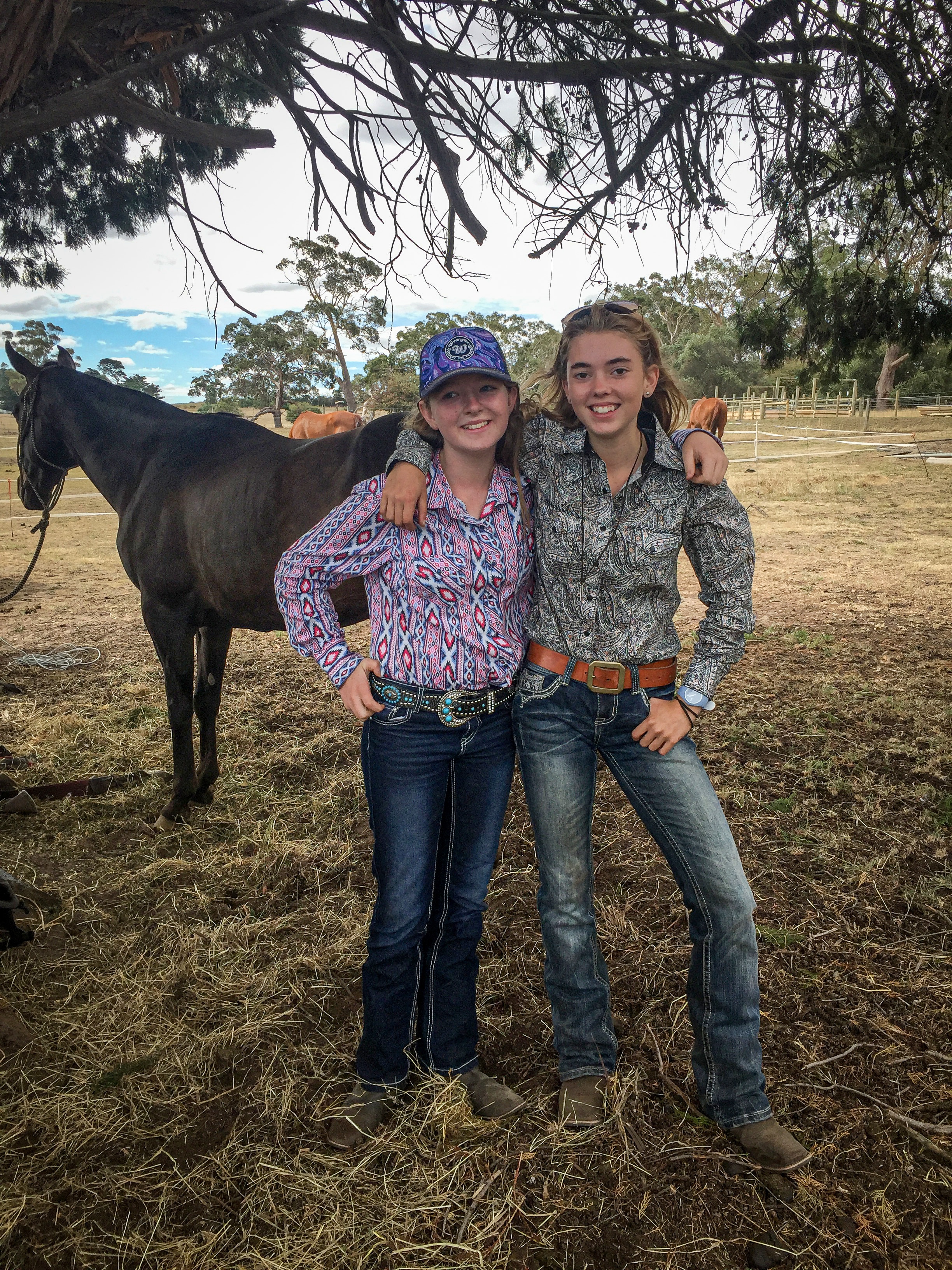 Two girls stand arm in arm in front of a horse