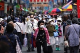 A street is crowded by shoppers wearing face masks