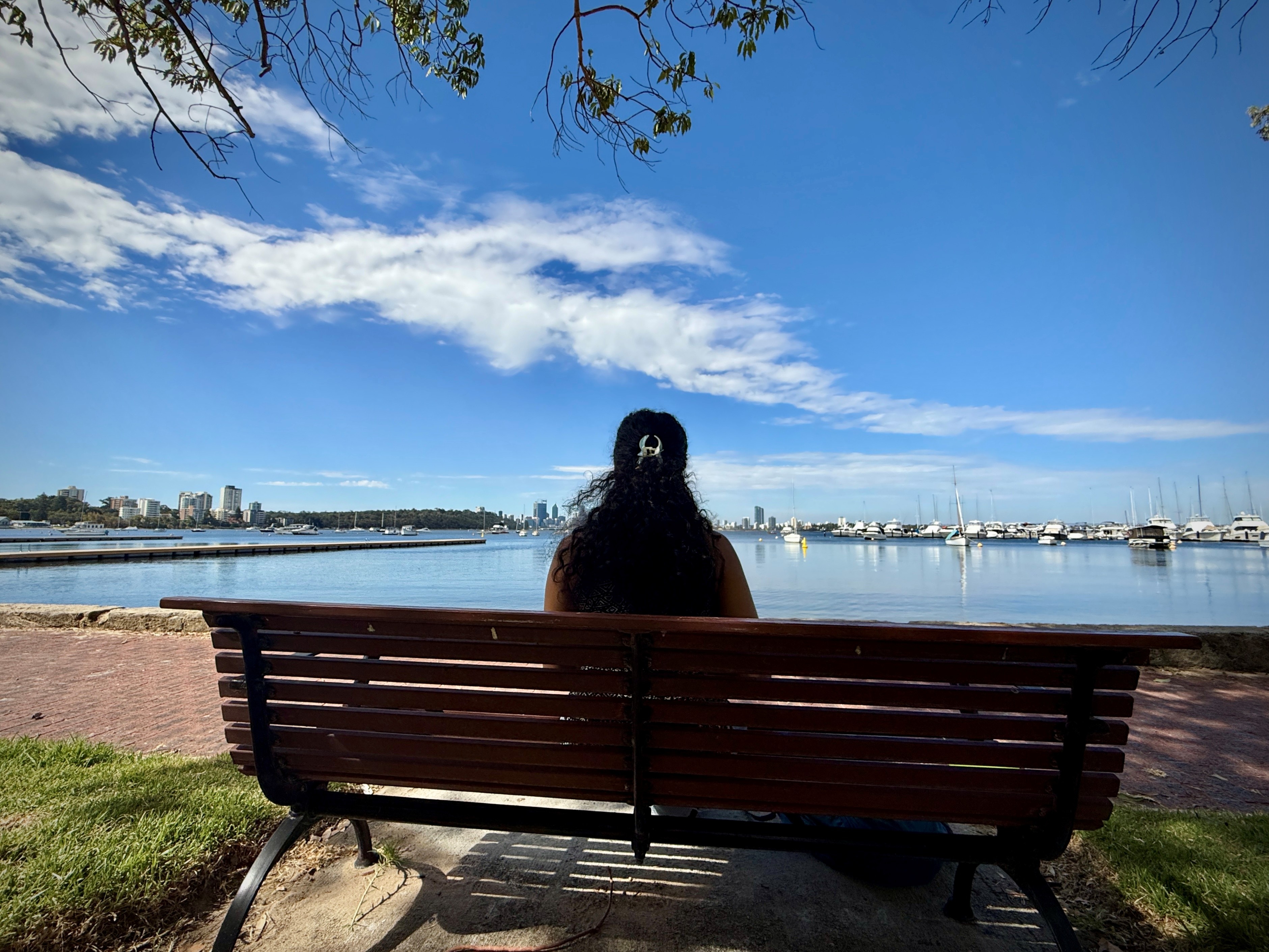 a young woman sits on a becnh overlooking the water