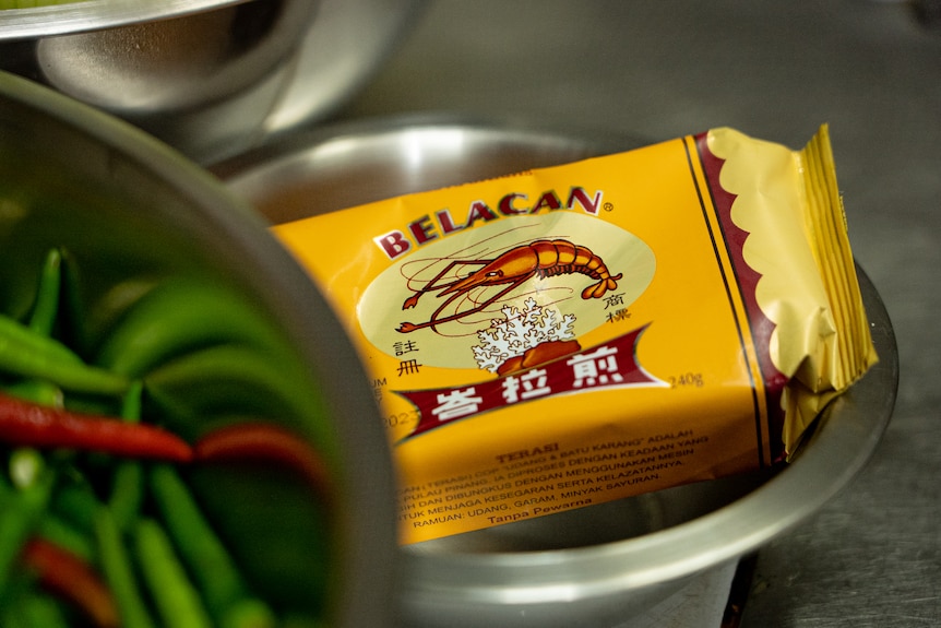A mustard coloured block of packaged shrimp paste sits on a bench. It reads Belacan.