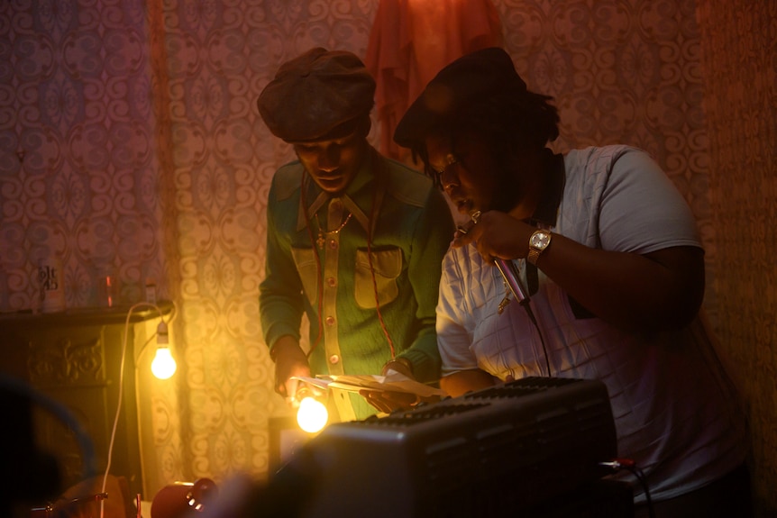A still from the film Lovers Rock with actors Kadeem Ramsay and Alexander James-Blake DJ-ing at a party