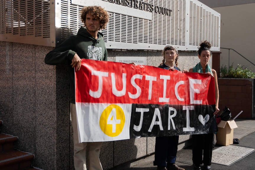 A few protestors outside of a court building with large signs that say "Justice for Jari".