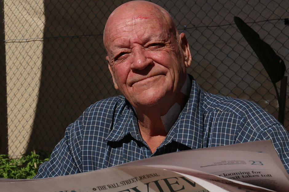 A man reads a newspaper, sitting in full sun.