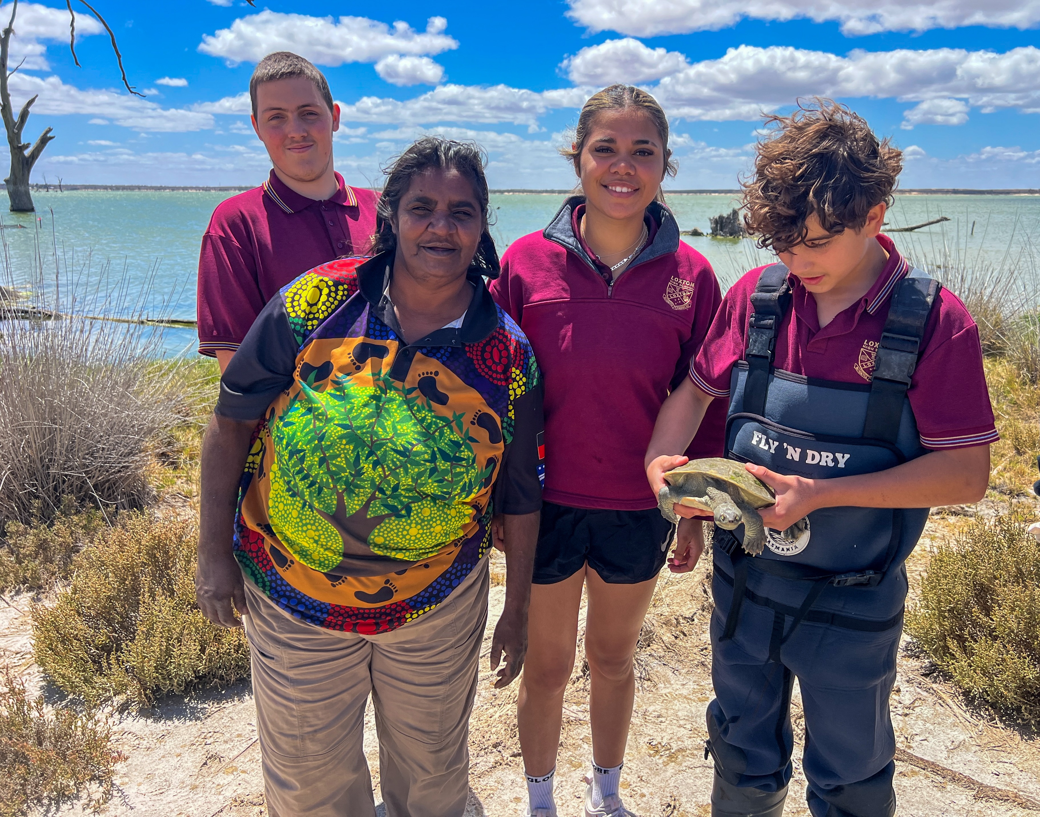 Un guardabosques indigno con estudiantes en un lago sosteniendo una tortuga.