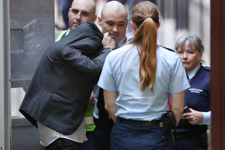A man with his face hidden by his jacket is escorted into court by security guards.