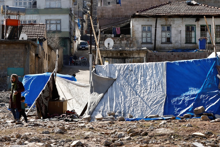 Tens surroundsed by rubble in front of houses. 