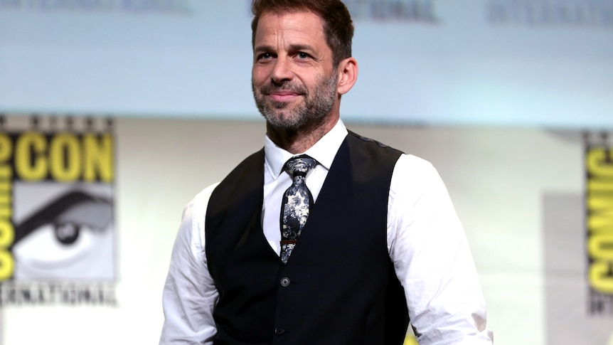 A man smiles while on stage at a Comic Con event.