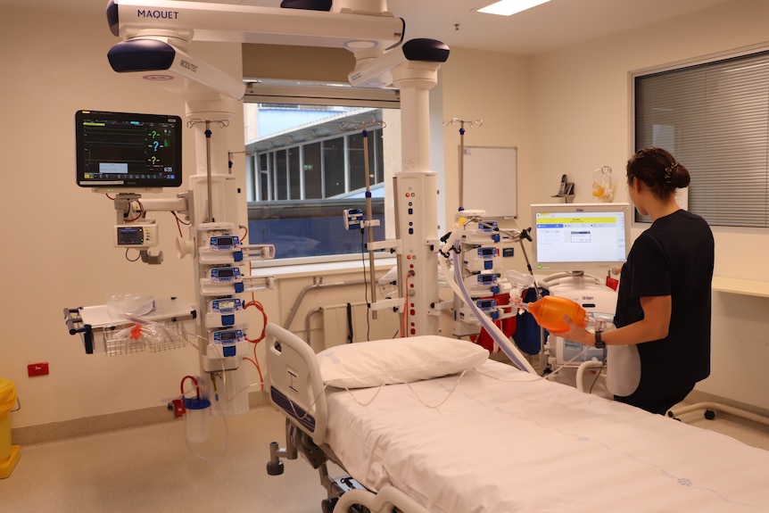 A woman dressed in scrubs stands next to a hospital bed.