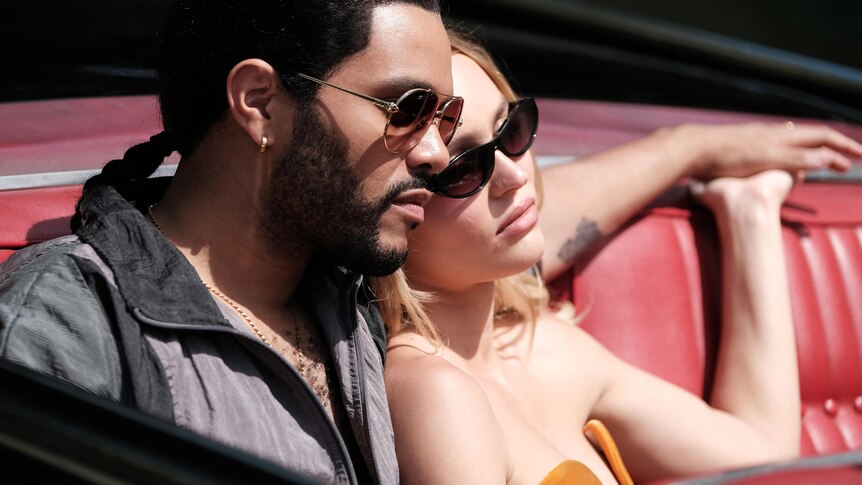 Abel has his arm around Lily-Rose as they sit in the red leather backseat of a convertible, wearing sunglasses.
