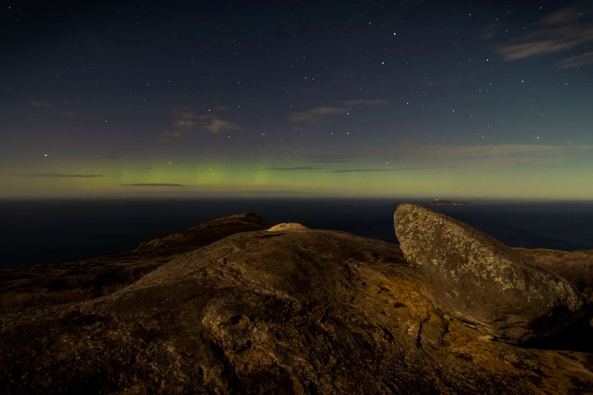 Green and pink colours light up the horizon, with rocks in the foreground near Albany in southern WA