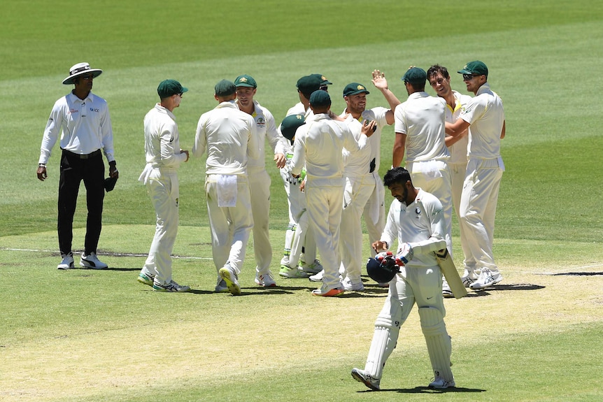 Australian cricketers high-five and hug as Indian batsman Jasprit Bumrah trudges past them.