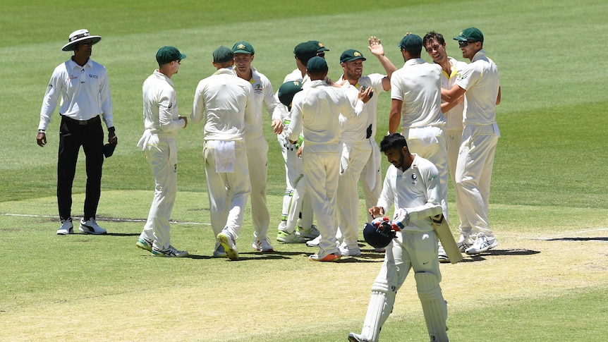 Australian cricketers high-five and hug as Indian batsman Jasprit Bumrah trudges past them.